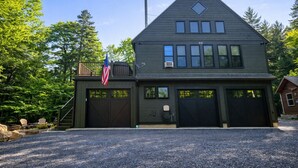 A two-story building with a garage, a flag, and a staircase leading to a deck. - Woods All Around-Direct ATV*Hot Tub*Beach Access*A/C*Pool Table*Washer/Dryer (Beaver Cove)