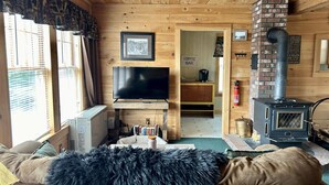 Un intérieur de chalet chaleureux et accueillant, avec un téléviseur, une cheminée, un coin café et un canapé agrémenté d’un plaid en fourrure.