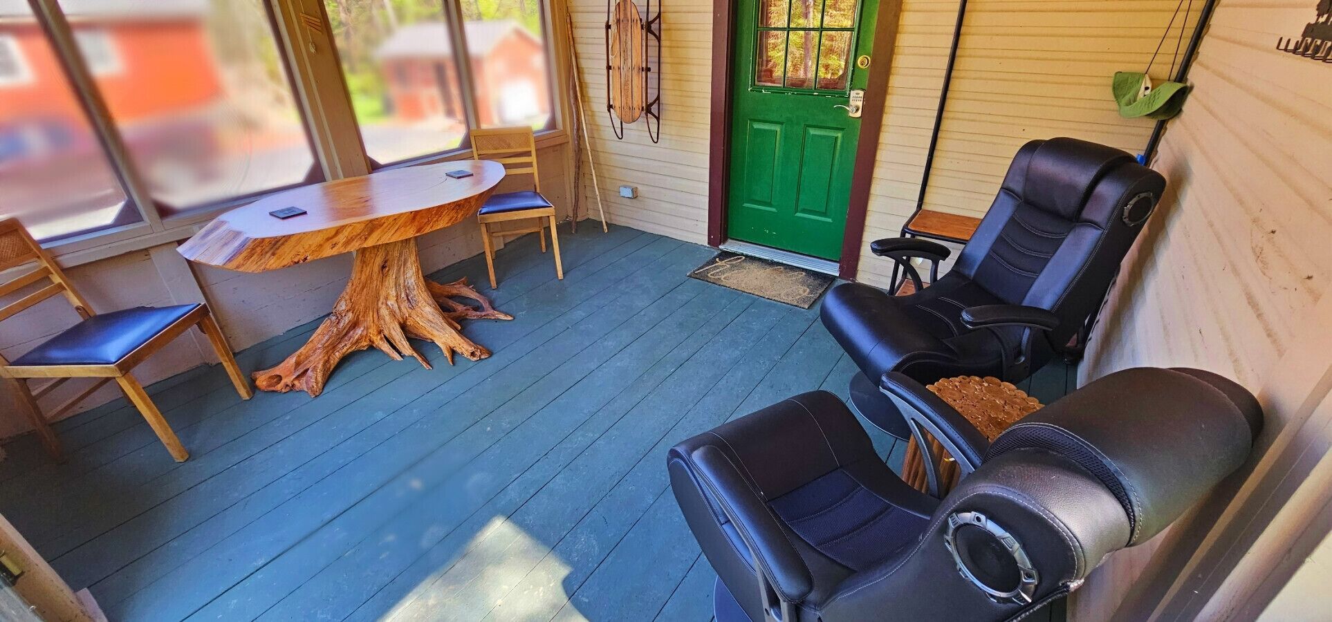 A cozy outdoor seating area with a wooden table and chairs, a large tree stump, and a green door.