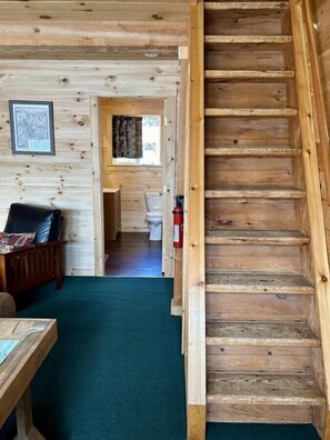 Een houten interieur met een trap, een houten bank, een tafel en een lijst met een foto aan de muur.
