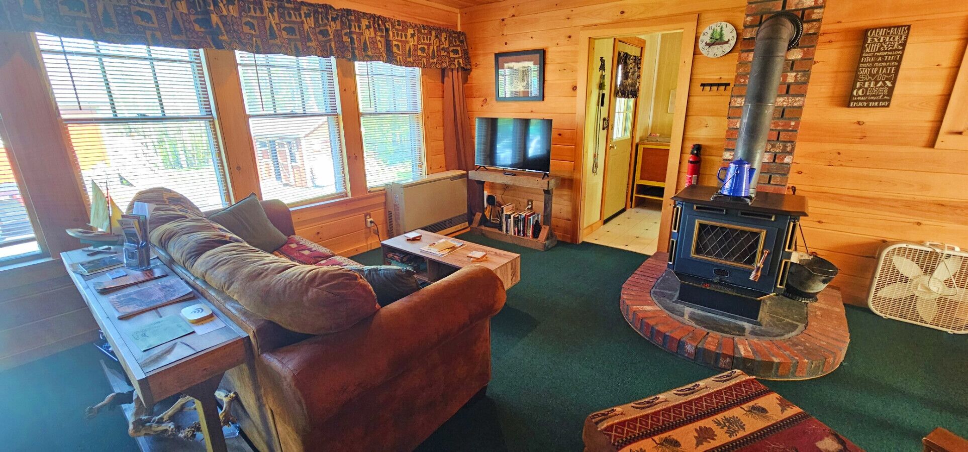 Interior acogedor de una cabaña con un sofá de cuero, un televisor, una chimenea y una estantería.