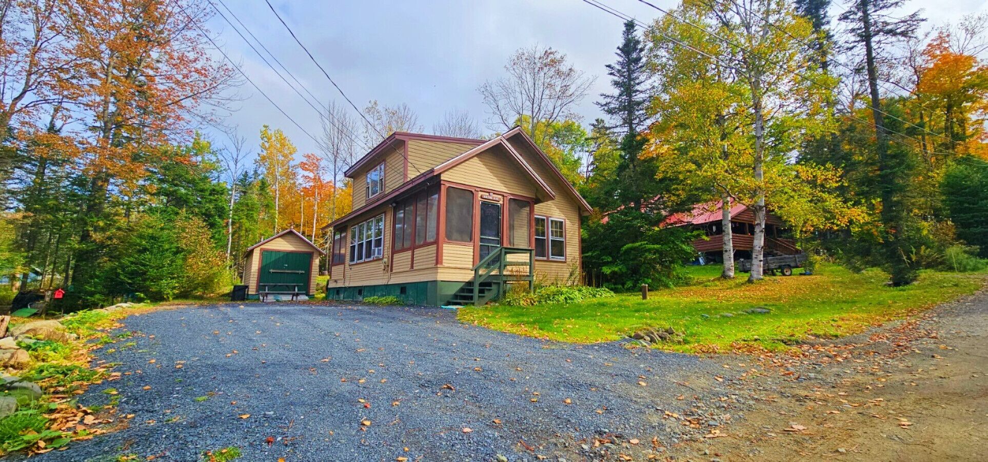 Une cabane à deux étages, dotée d’un porche à l’avant et d’un garage, entourée d’un feuillage automnal.