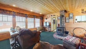 L’intérieur chaleureux d’un chalet avec un plafond en bois, une cheminée, un canapé et un téléviseur.