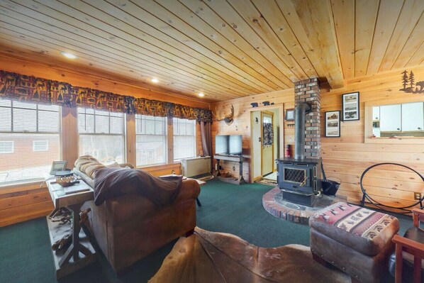A cozy cabin interior with a wooden ceiling, a fireplace, a sofa, and a television.