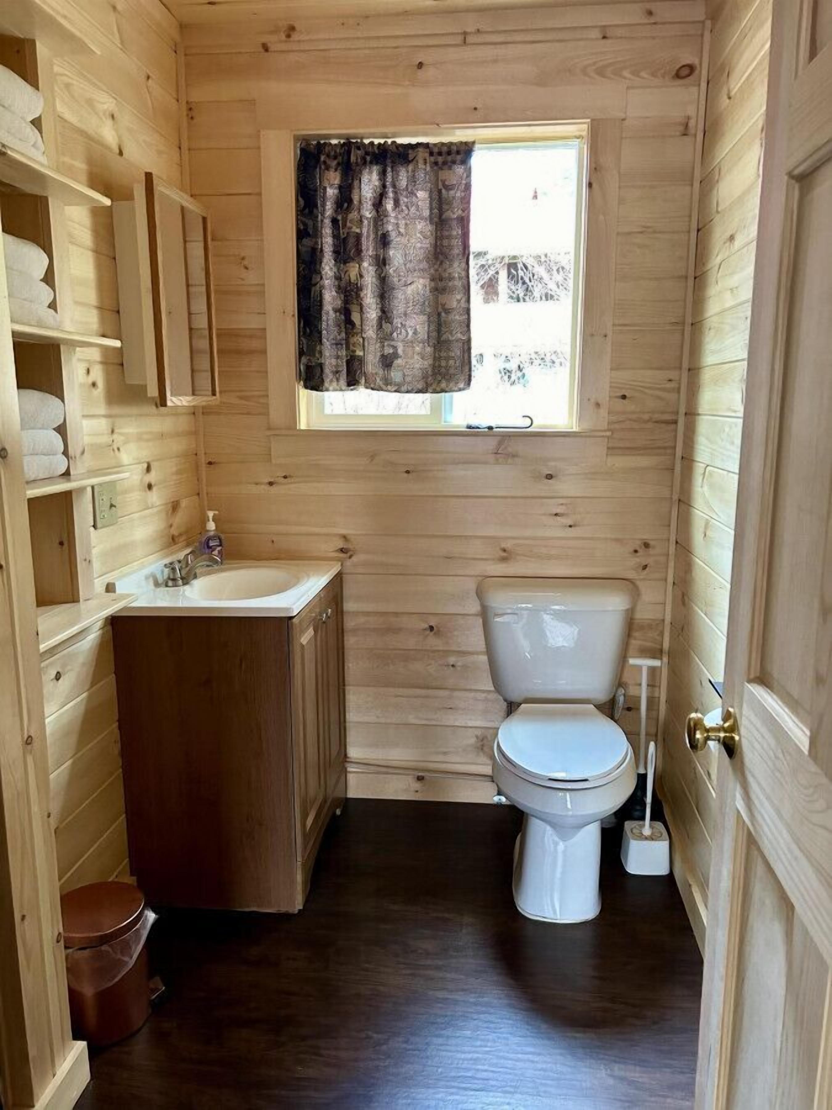 Ein kleines, hölzernes Badezimmer mit Toilette, Waschbecken und Stauraumschränken.