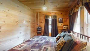 Une pièce de cabane en bois comprenant un lit, une fenêtre avec des rideaux et une petite table avec une lampe.