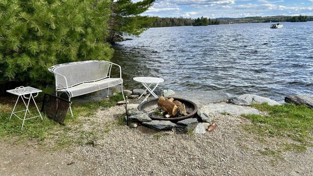 Un endroit au bord du lac, avec un banc en métal, une petite table et un foyer.