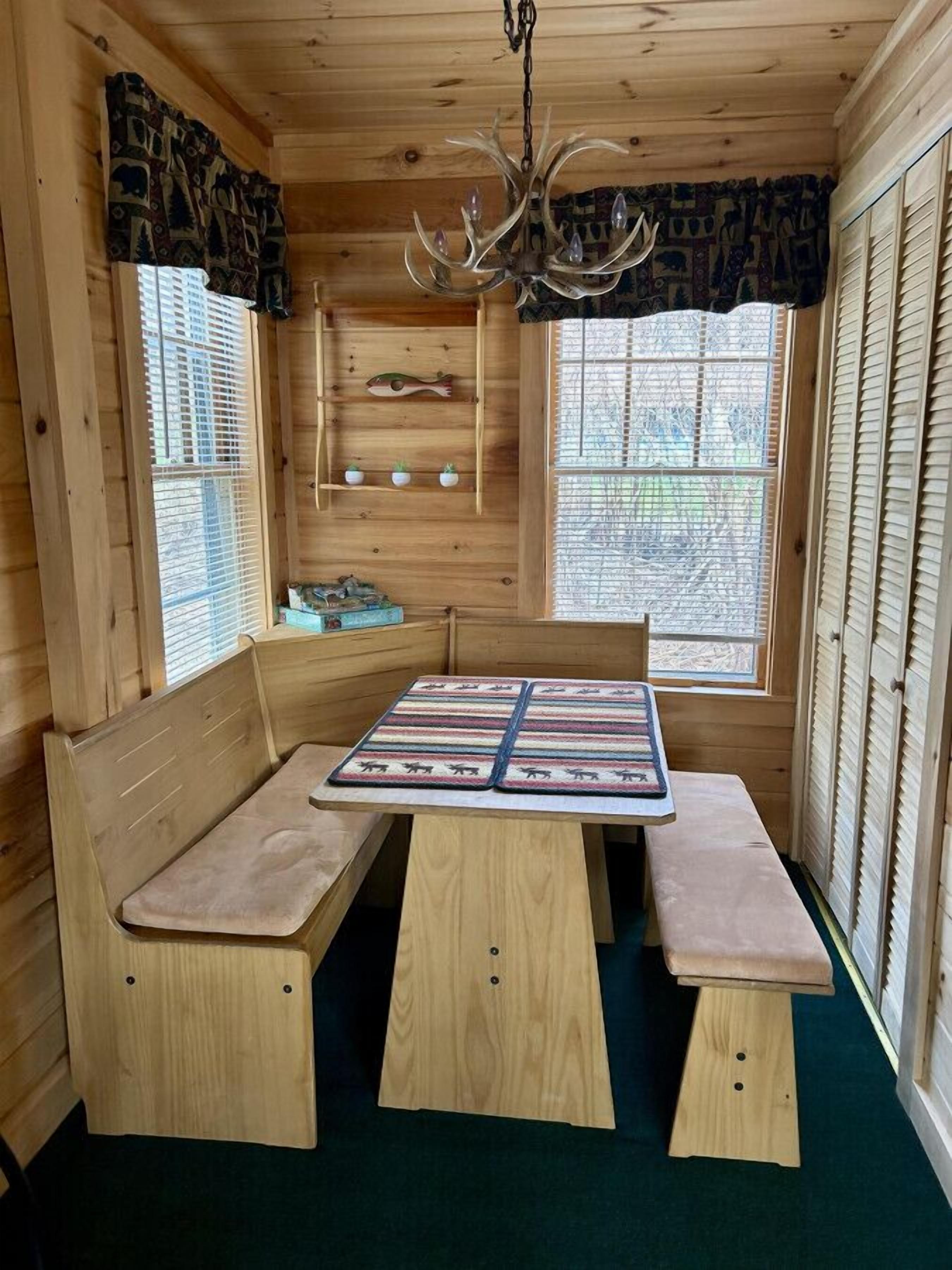 L’intérieur chaleureux d’un chalet avec un banc en bois servant de coin salon, une table agrémentée d’un set de table coloré et un lustre.