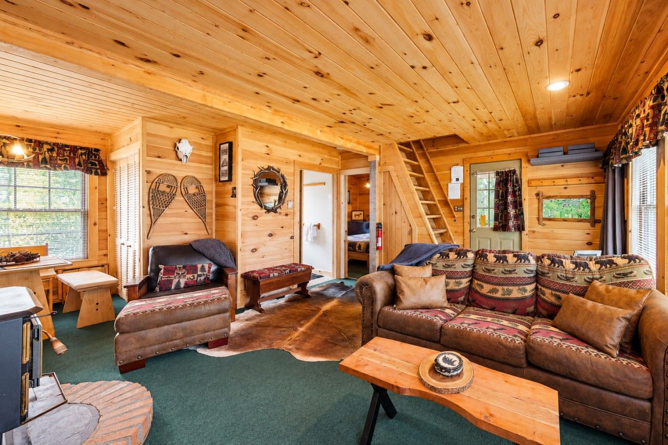 A log cabin interior with a fireplace, leather sofa, and a dining area.