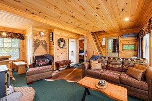 L’intérieur d’une cabane en rondins, avec une cheminée, un canapé en cuir et un coin repas.