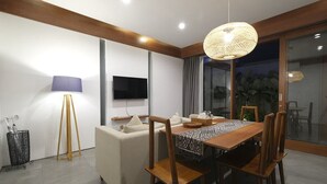 Ein moderner Essbereich mit einem Holztisch, Stühlen, einem Fernseher und einem großen Fenster mit Blick auf Grünflächen.