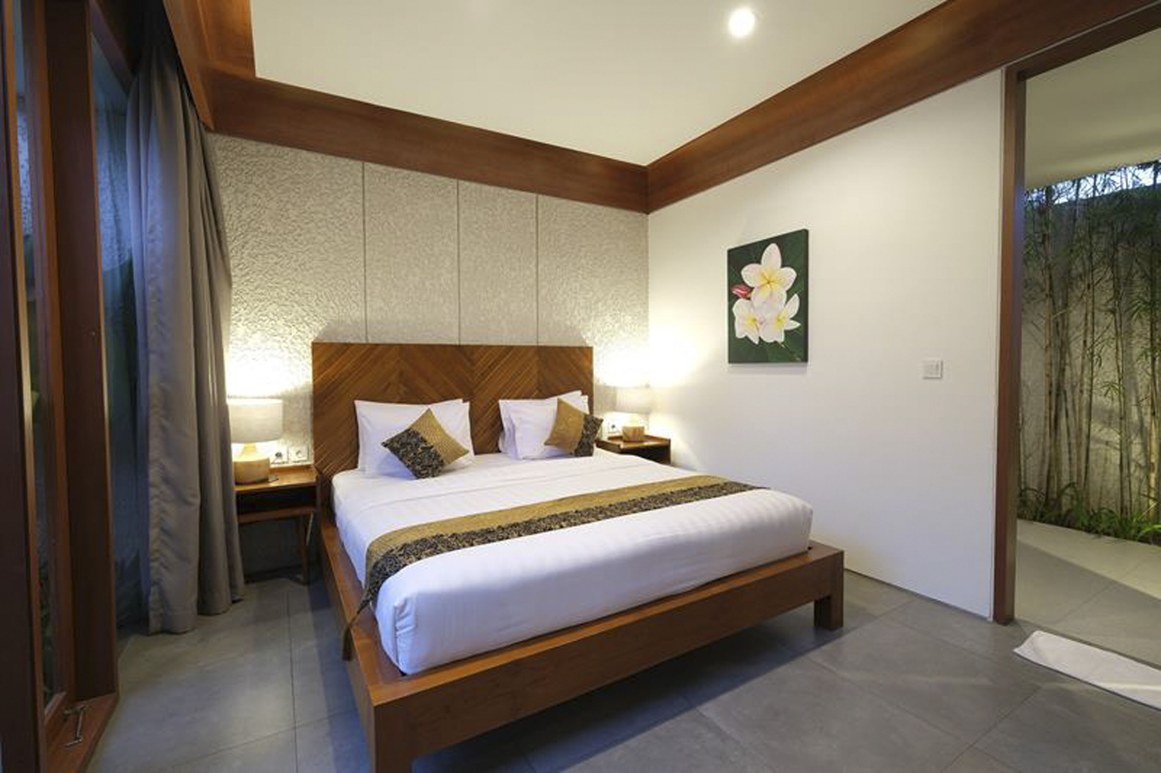 Een moderne hotelkamer met een groot bed, een houten hoofdeinde en een nachtkastje met een lamp.