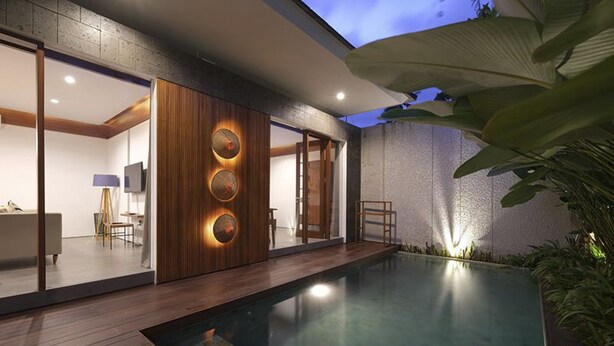 Ein modernes Haus mit Schwimmbad, Holzterrasse und einer großen Pflanze.