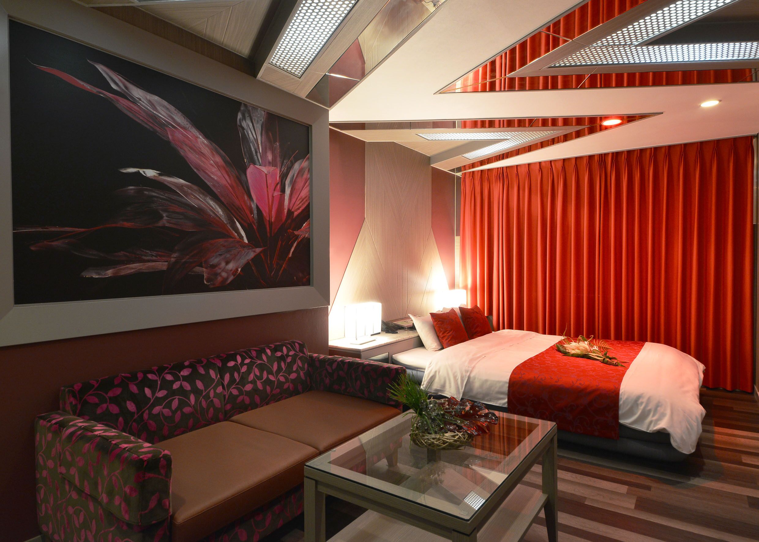 Una habitación de hotel moderna con una cama grande, un sofá, una mesa de centro de vidrio y una obra de arte en la pared.