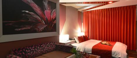Una habitación de hotel moderna con una cama grande, un sofá, una mesa de centro de vidrio y una obra de arte en la pared.