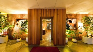 Un vestíbulo de hotel con un mostrador de recepción de madera, plantas en macetas y una alfombra roja que conduce a la entrada.