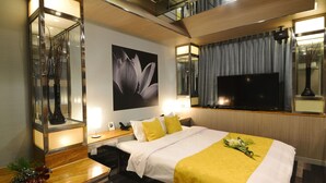 Una habitación de hotel moderna con una cama grande, un televisor de pantalla plana, una mesita de noche con lámpara y un espejo decorativo.