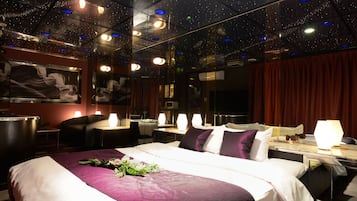 A modern hotel room with a large bed, a desk, and a chair. The room has a starry ceiling and a large mirror on one wall.