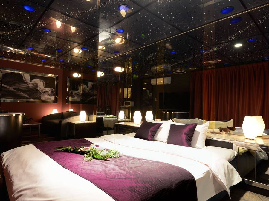 A modern hotel room with a large bed, a desk, and a chair. The room has a starry ceiling and a large mirror on one wall.
