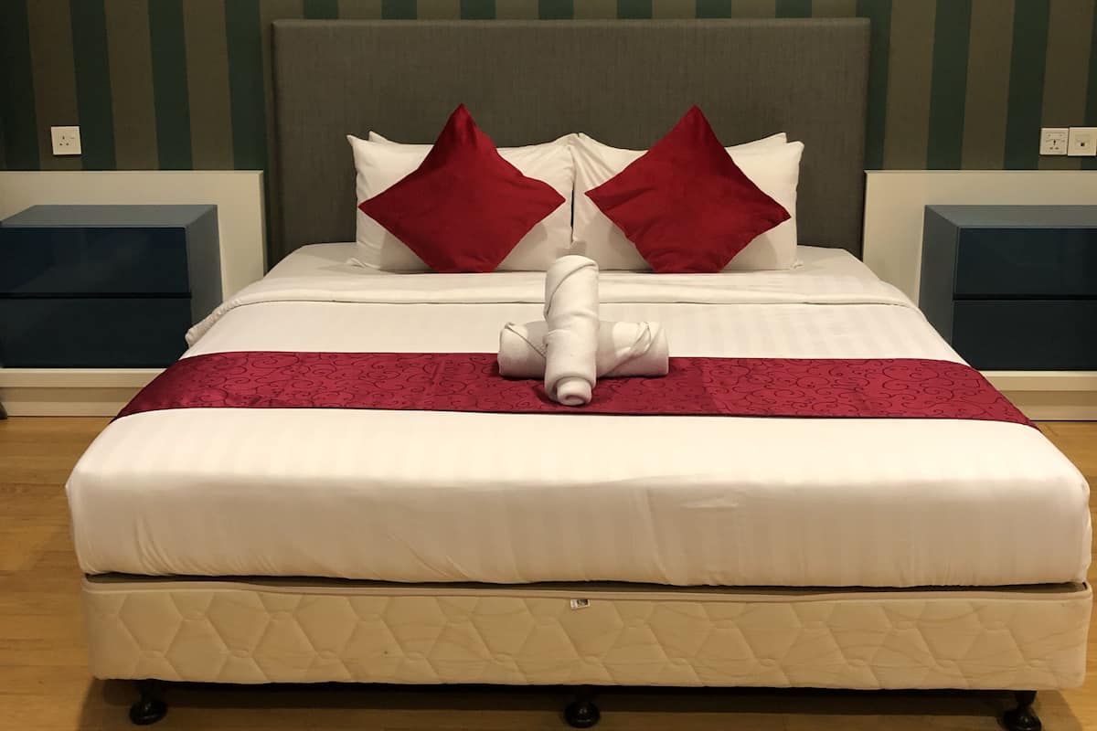 A neatly made bed with a red and white bedspread, two red pillows, and a rolled towel.