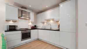 A modern kitchen with white cabinetry, a microwave, stove, oven, and a sink. - Park Place Court 2 - Close to Beach (Tenby)