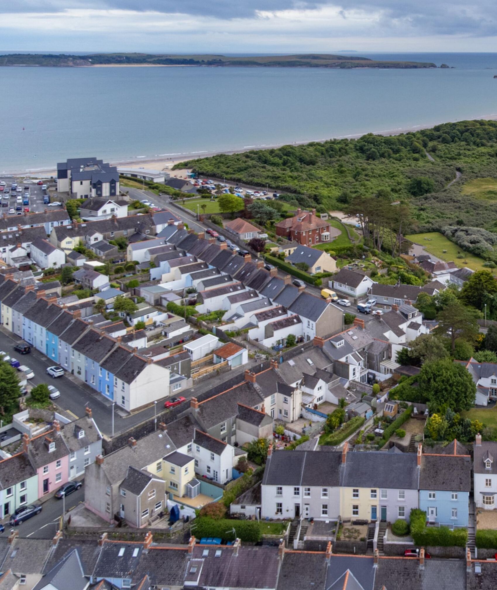 A coastal residential area with terraced houses, a beach, and a hilly landscape in the background.