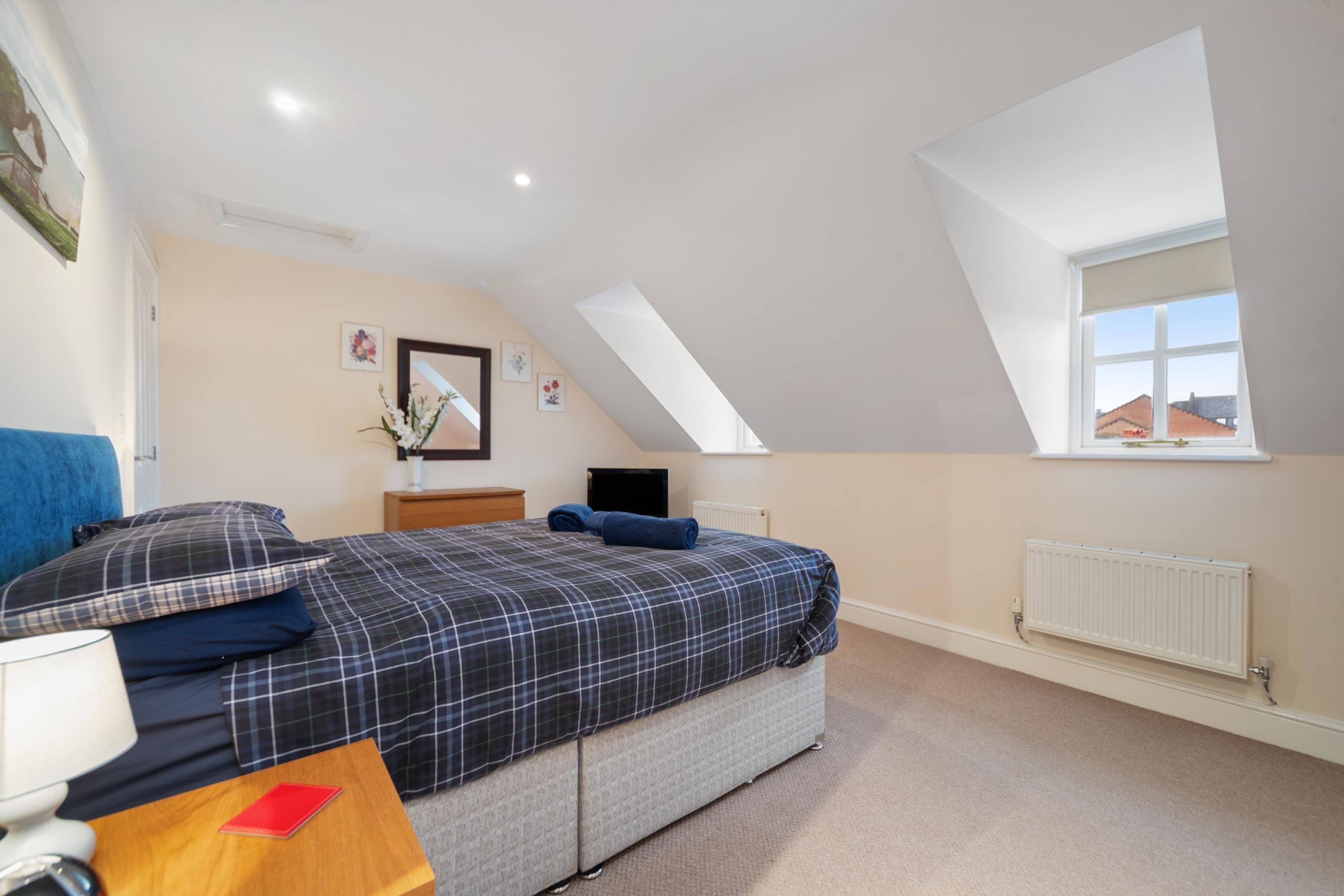 A bedroom with a bed, a nightstand, a lamp, a radiator, and a window with a view of buildings.