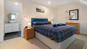 A bedroom with a bed, bedside tables, a dresser, a mirror, and artwork on the walls. - Park Place Court 2 - Close to Beach (Tenby)