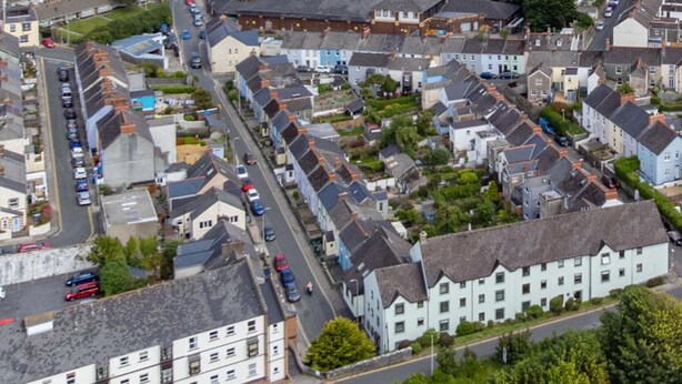 Une ville côtière où se côtoient des immeubles résidentiels et commerciaux, une église dont le clocher est particulièrement visible, et un grand parking.
