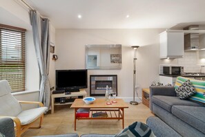 A modern living room with a flat-screen TV, a fireplace, a sofa, and a dining table. - Park Place Court 2 - Close to Beach (Tenby)