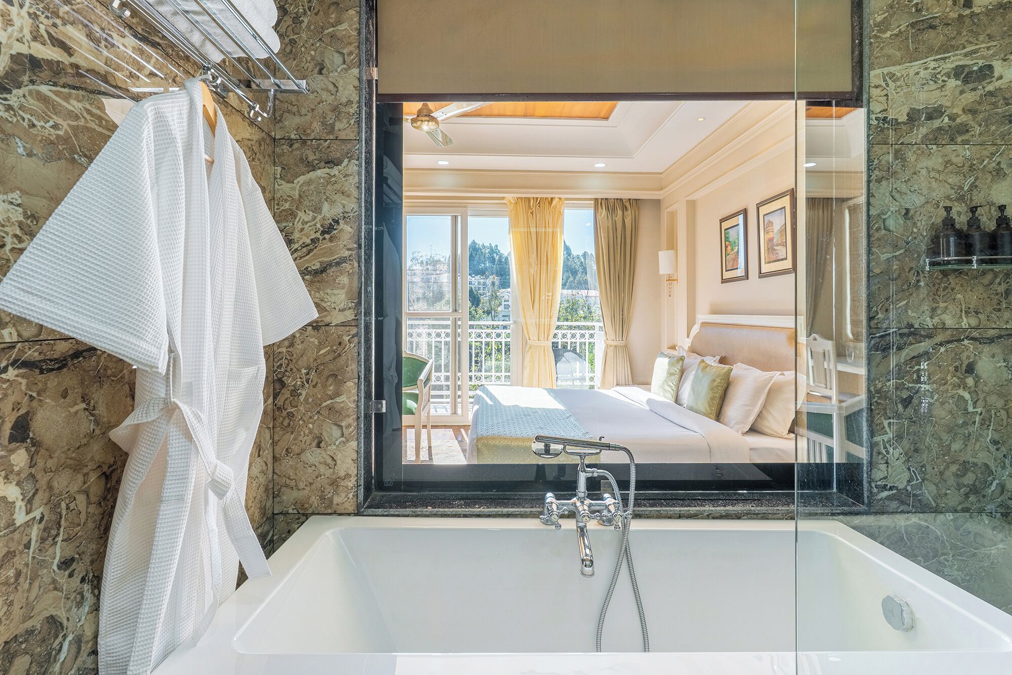 A bathroom with a large bathtub, a towel rack, and a view of a balcony with a bed.