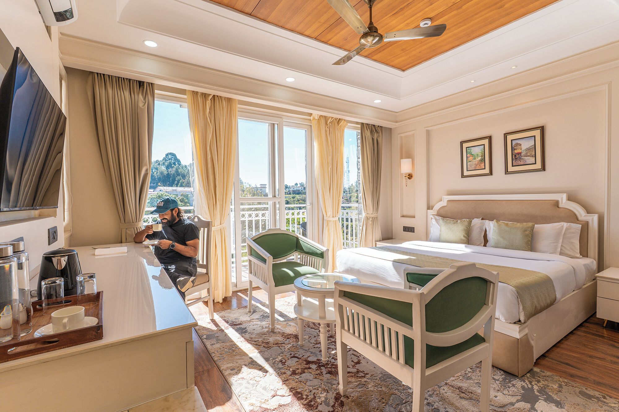 A hotel room with a bed, a desk with a coffee maker, a chair, and a balcony with curtains.