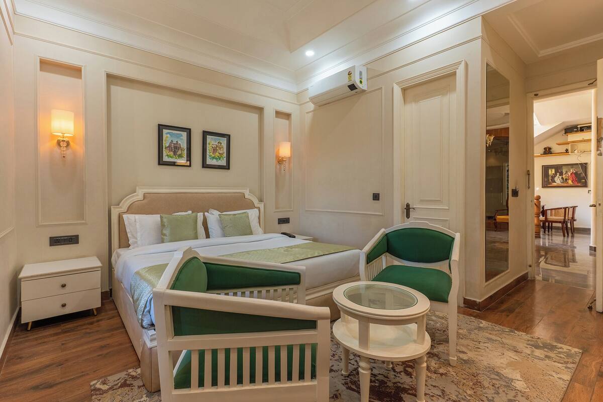 A hotel room with a bed, a chair, a small table, and a painting on the wall.
