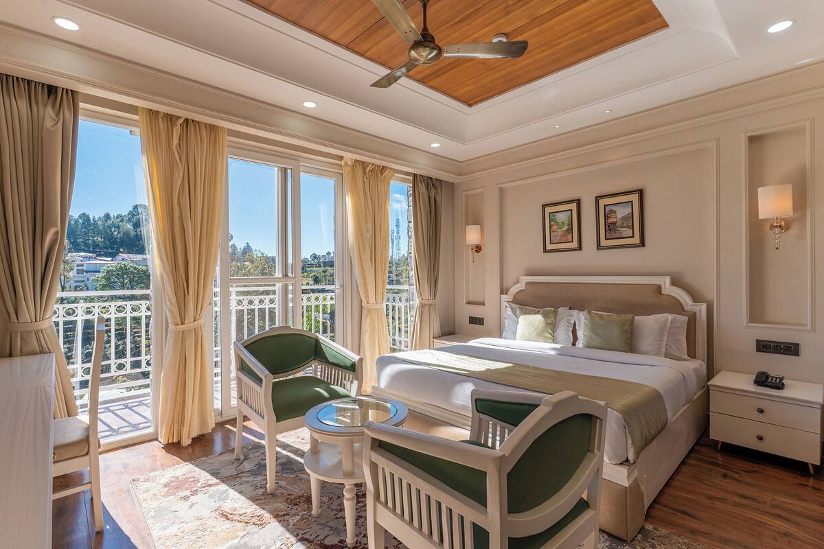 A hotel room with a bed, a chair, a small table, and a balcony with curtains.