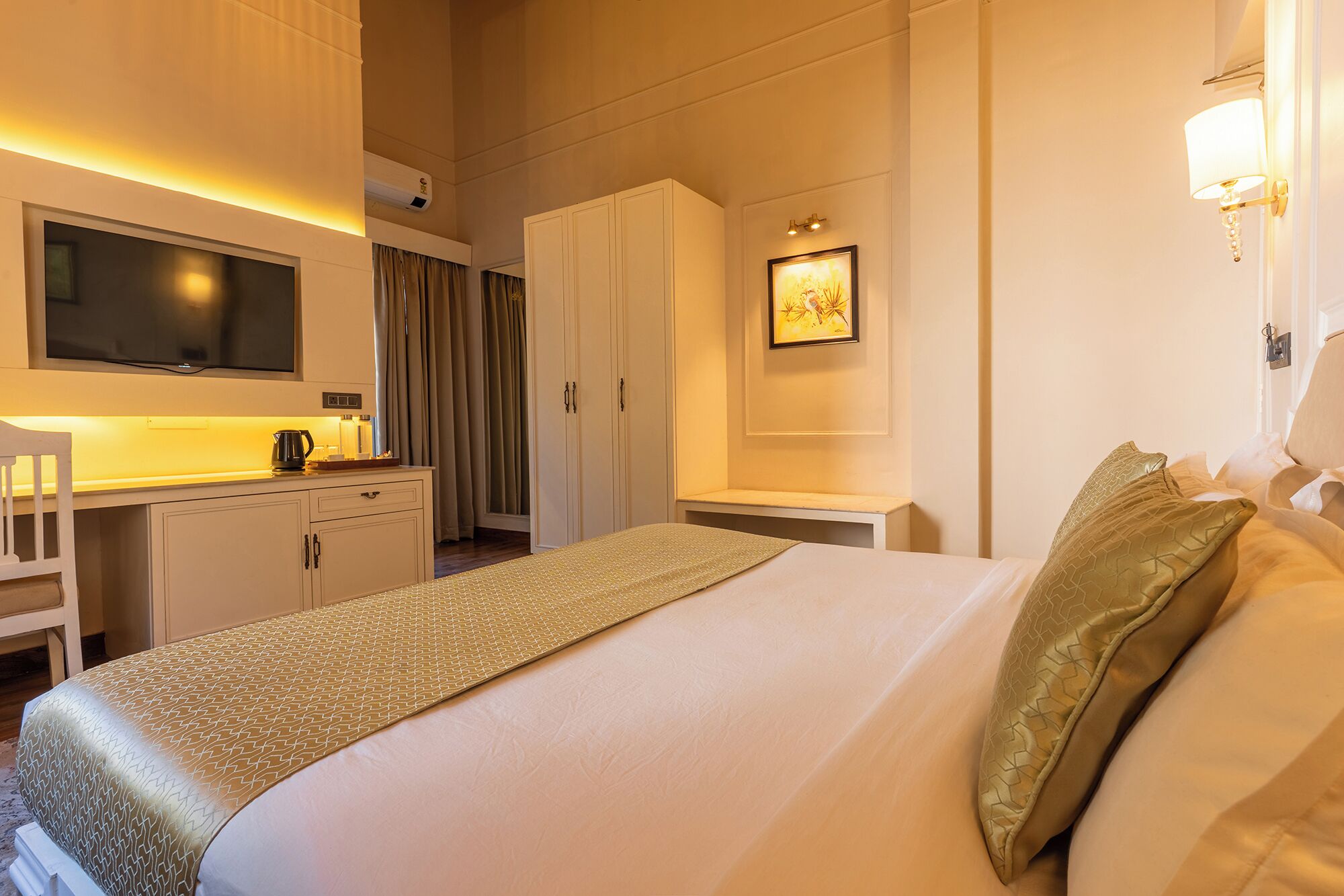 A hotel room with a bed, a desk with a kettle, a television, and a wardrobe.