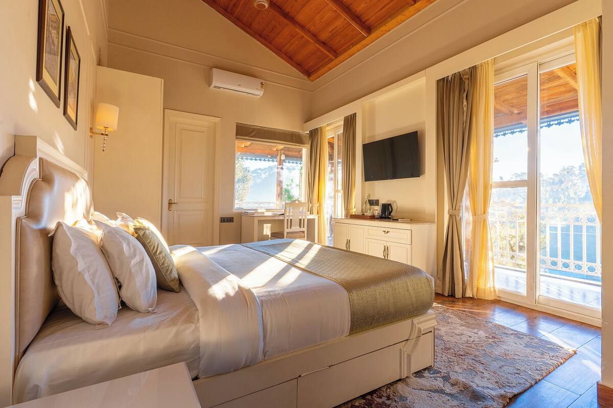 A bedroom with a bed, a desk, a TV, and a balcony with curtains.