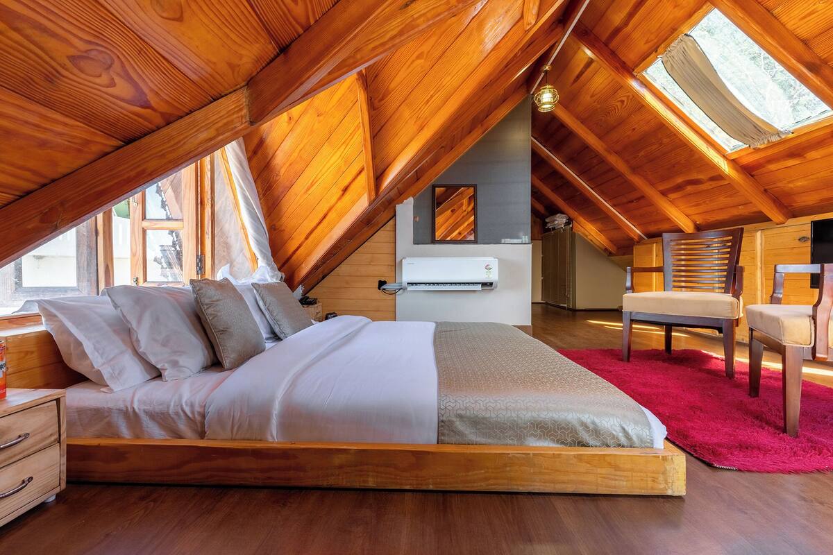 A bedroom with a wooden ceiling, a bed, a chair, and a red rug.