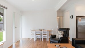 Una sala de estar moderna con una mesa de comedor de madera, sillas blancas, un sofá de cuero negro y un refrigerador.
