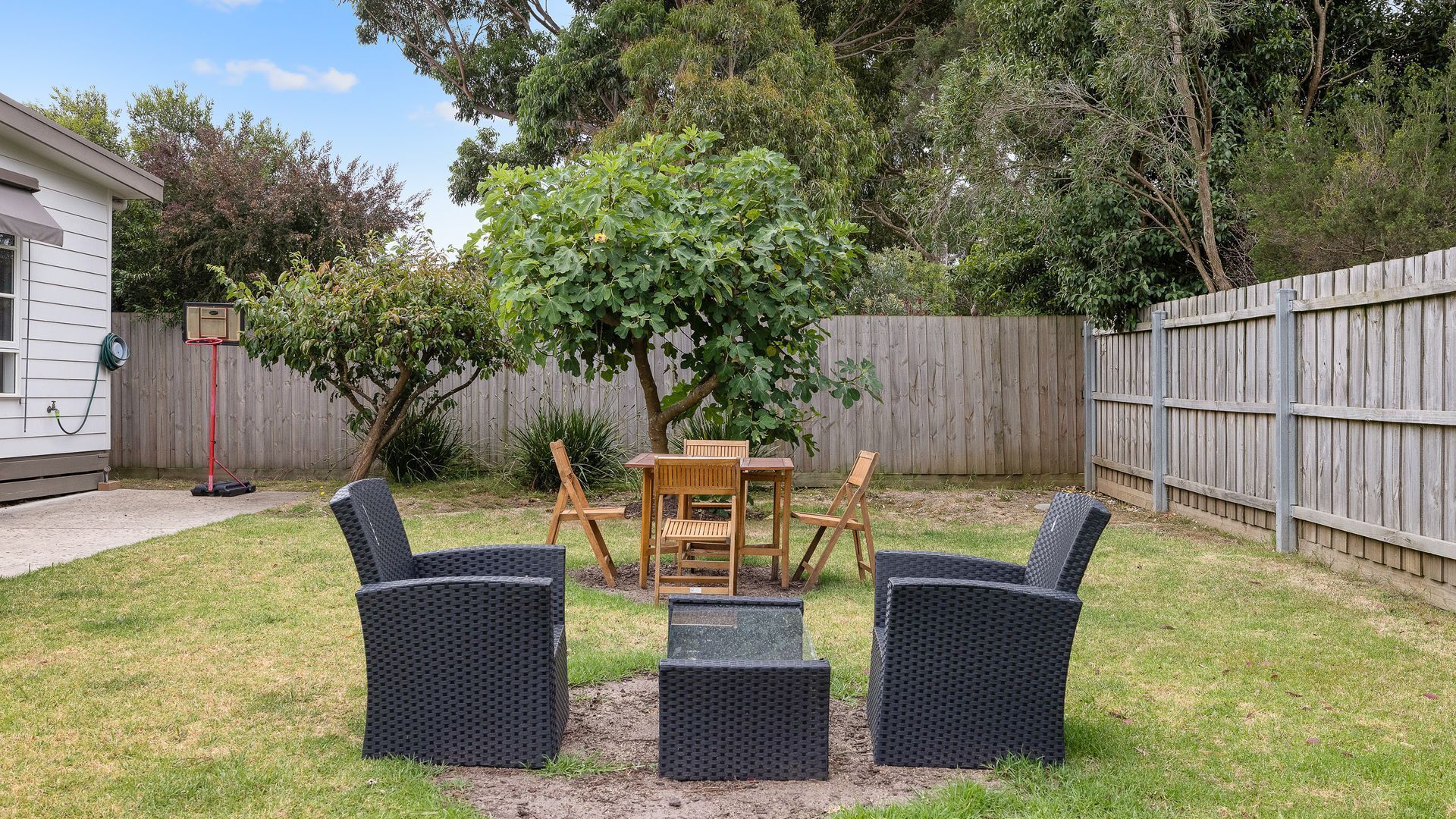 A backyard with a wooden table and four chairs, surrounded by a wooden fence and trees.
