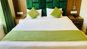 A hotel room with a bed, green pillows, a green quilt, a wooden headboard, a bedside table with a phone, and a nightstand. - Hotel Global Inn (Amritsar)