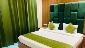 A hotel room with a green upholstered headboard, white bedding, and a green throw blanket. - Hotel Global Inn (Amritsar)