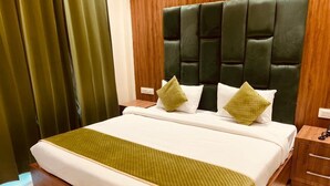 A neatly made bed with a green quilt, a dark upholstered headboard, and two bedside tables with lamps. - Hotel Global Inn (Amritsar)