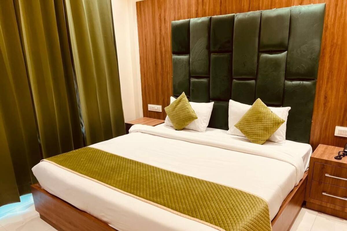 A neatly made bed with a green quilt, a dark upholstered headboard, and two bedside tables with lamps.