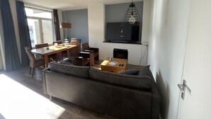 Ett modernt vardagsrum med en soffa, ett matbord, stolar, en öppen spis och en tv som är monterad på väggen.