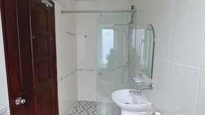 Een badkamer met een zwart-wit geruite vloer, een houten deur, een glazen douchecabine, een wastafel met spiegel en een toilet.