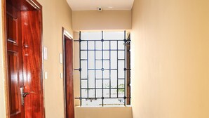 A hallway with a wooden door, a window with metal bars, and a tiled floor. - West Suites Apartments (Nairobi)