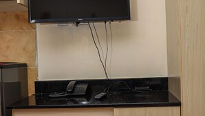 A small kitchenette with a black countertop, a built-in stove, a wall-mounted TV, a phone, and a cabinet with two drawers. - West Suites Apartments (Nairobi)