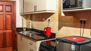 A kitchen with wooden cabinets, a black stove, a red kettle, and a microwave. - West Suites Apartments (Nairobi)