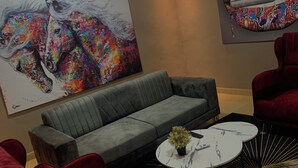 A modern lounge area with a grey sofa, red armchairs, a white coffee table with a plant, and two large abstract paintings on the walls. - Magic City Apartment (Kasoa)