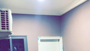 A room with a white door, a window with a decorative pattern, and an air conditioning unit on the wall. - Magic City Apartment (Kasoa)